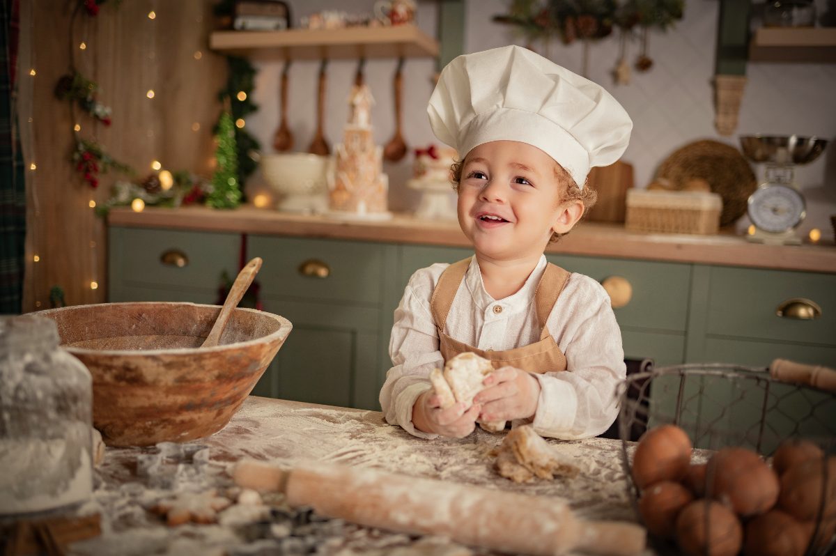 Un niño con gorro de cocinero sonríe con la masa en las manos.